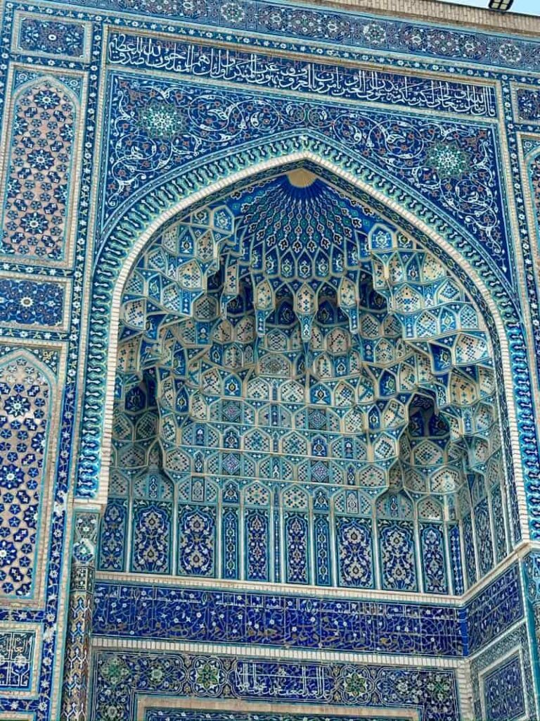 A close-up macro shot of the historic mosaic tilework at the Shah-i-Zinda Necropolis in Samarkand, Uzbekistan, showcasing intricate geometric patterns rendered entirely in shades of cobalt blue, turquoise, white, and beige.