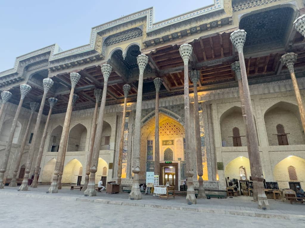 Front view of the historic Bolo Hauz Mosque in Bukhara, Uzbekistan, featuring its famous tall, intricately carved wooden pillars and ornate painted ceiling.