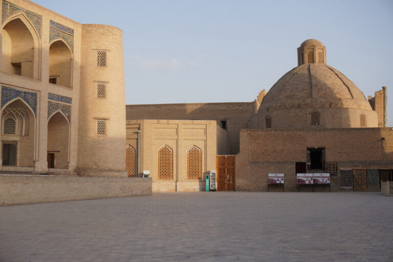 Panoramic landscape view of traditional brown brick buildings and rounded domes across the historic old town of Bukhara, Uzbekistan, bathed in the warm golden light of sunset.
