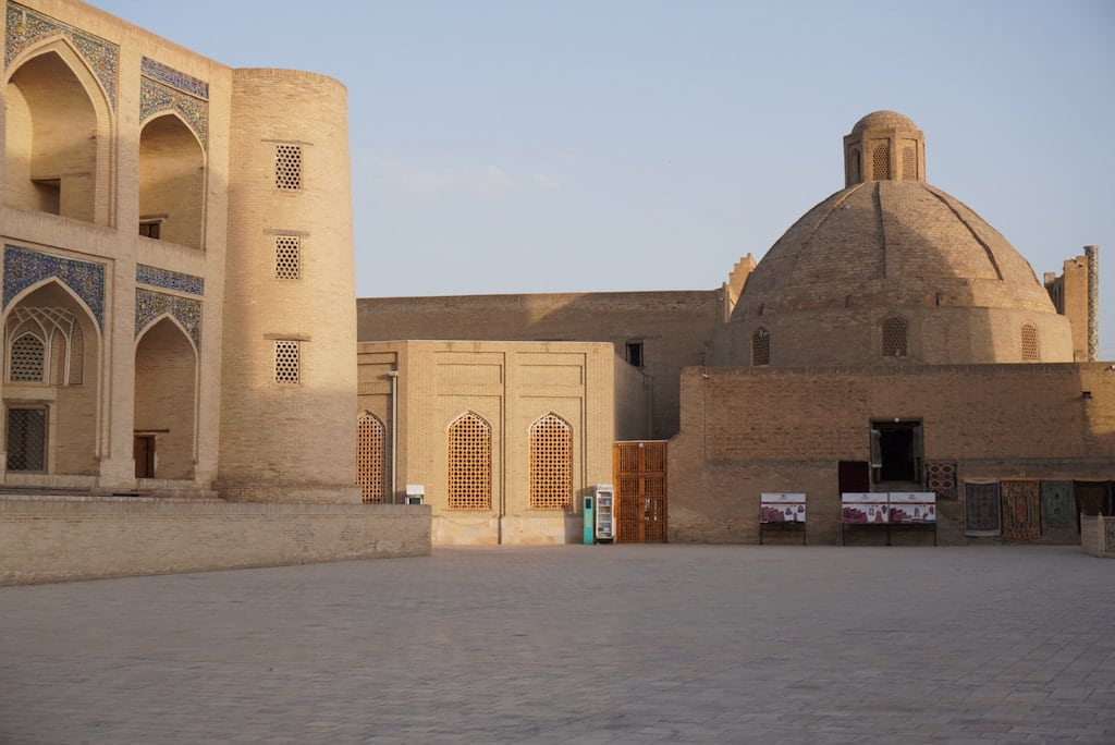 Panoramic landscape view of traditional brown brick buildings and rounded domes across the historic old town of Bukhara, Uzbekistan, bathed in the warm golden light of sunset.