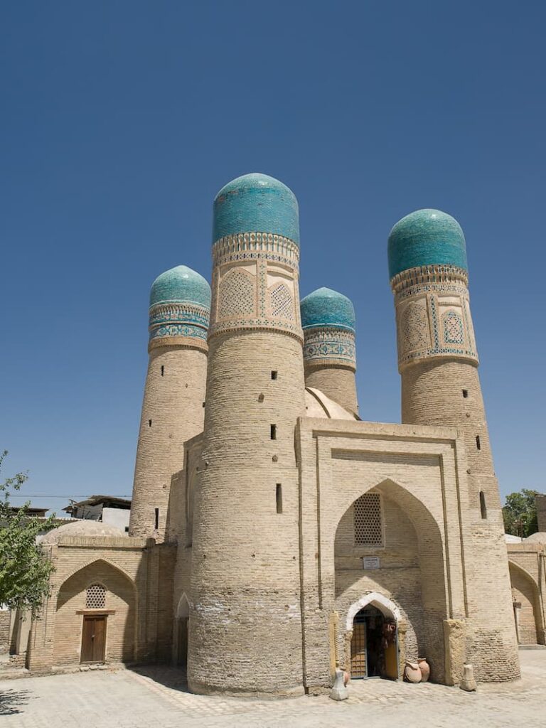 The historic Chor Minor Madrasah in Bukhara, Uzbekistan, featuring its four iconic turquoise-domed towers against a clear sky.