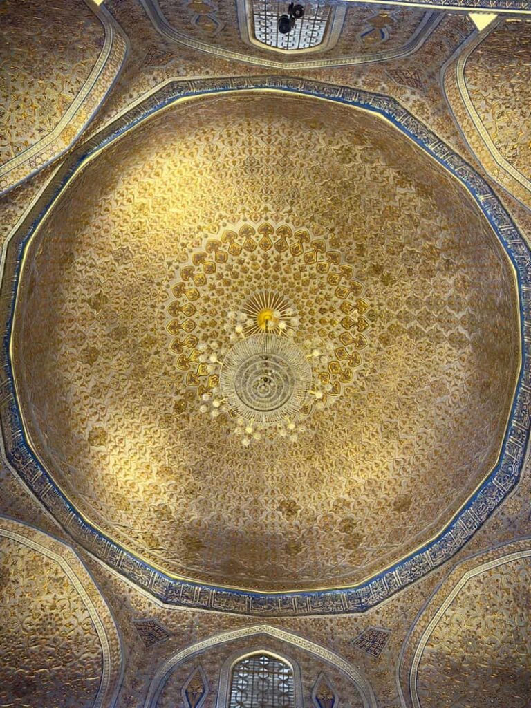 Looking directly up at the opulent golden dome interior and ornate hanging chandelier inside the Gur-e-Amir Mausoleum in Samarkand, Uzbekistan,