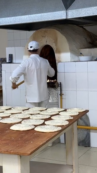 A local baker sticking fresh bread dough onto the inside wall of a traditional clay tandir oven to bake traditional Uzbek non bread
