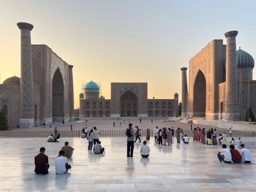 landscape view of the Registan Square during sunset showing people sitting down and enjoying the view of the madrasahs, Samarkand, Uzbekistan