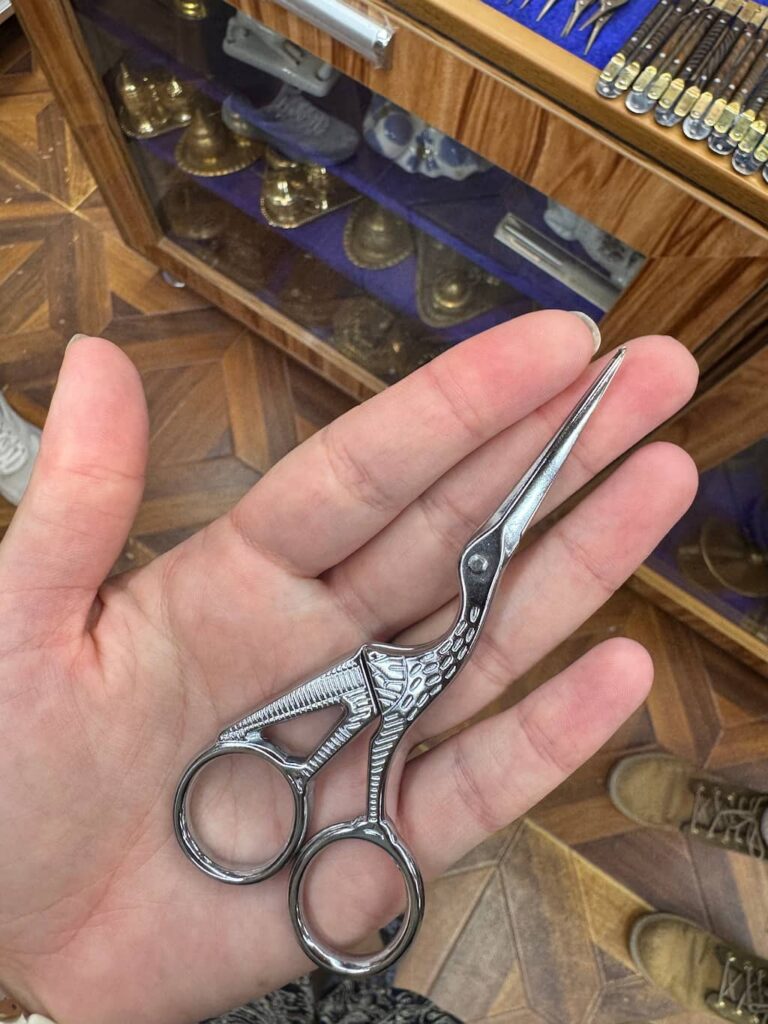 A close-up shot of the author holding a pair of traditional handmade Uzbek scissors intricately shaped like a stork bird in Bukhara.