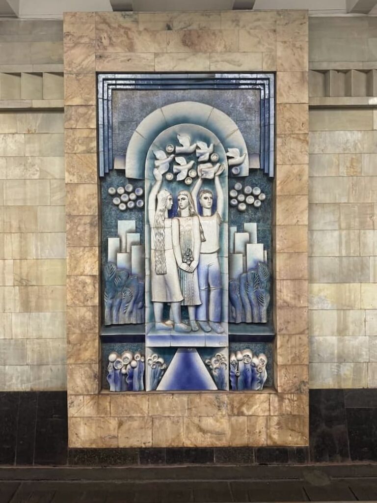 blue and white mosaic of three people holding white birds at tashkent metro station in tashkent, uzbekistan