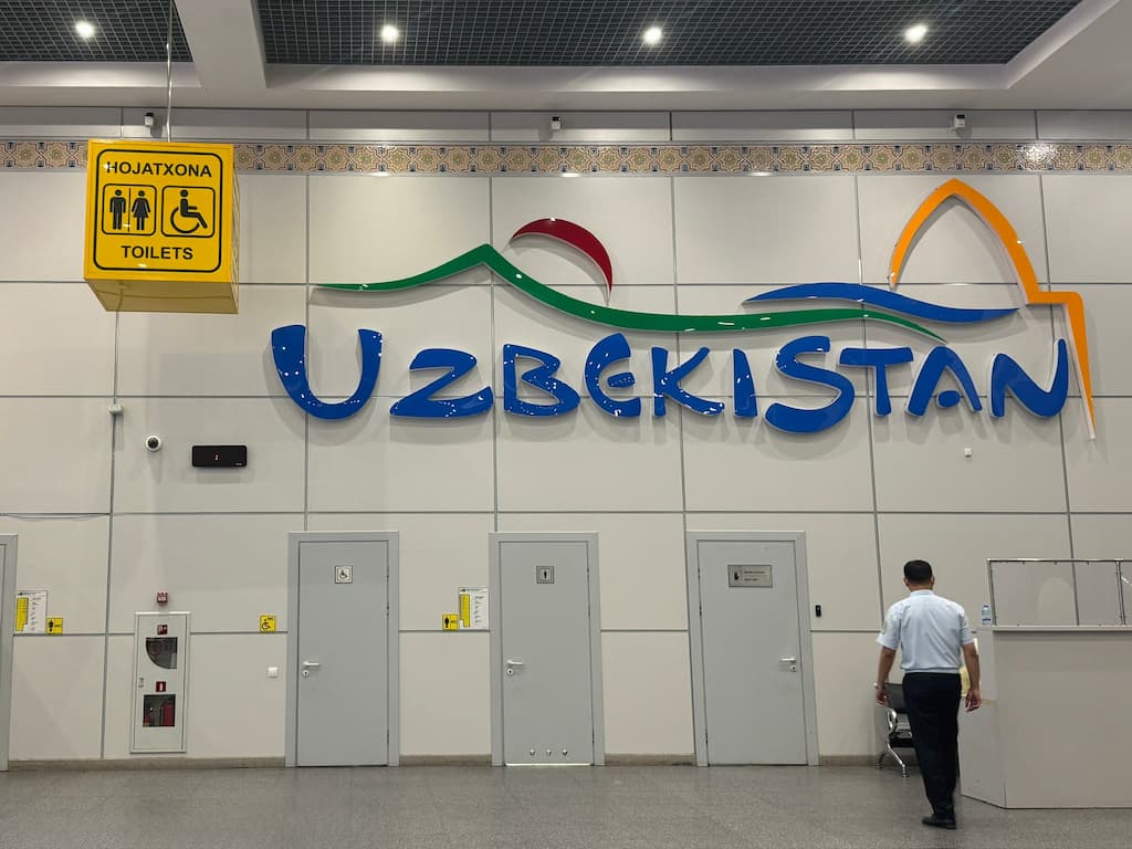 An image from our Uzbekistan travel guide showing the arrivals hall of an airport featuring a massive bright blue sign that reads 'Uzbekistan' with an airport employee walking toward it.