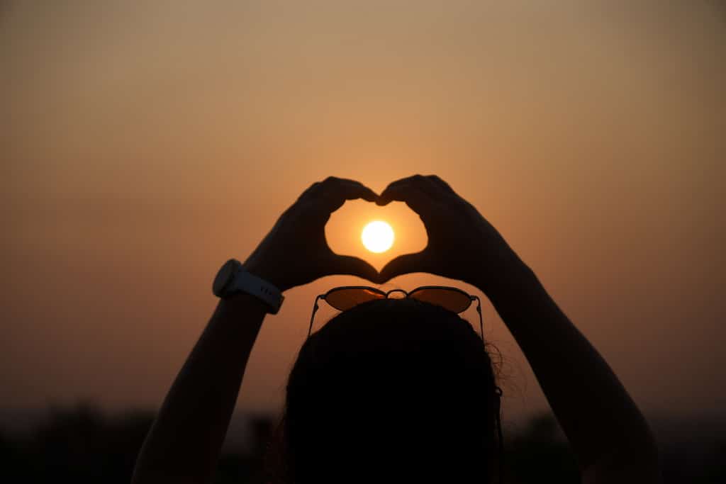 Traveler making a hand heart shape against a golden sunset sky in Angkor Wat, in Cambodia.