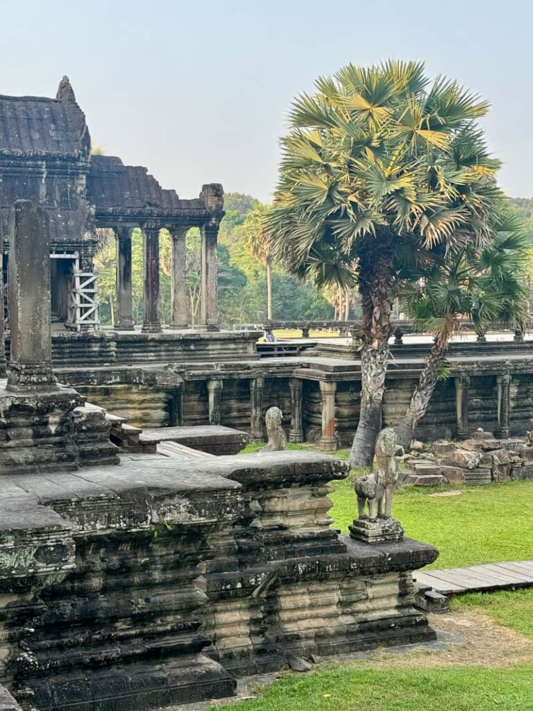 Historic stone ruins, guardian statues, and palm trees in the inner courtyard of Angkor Wat temple