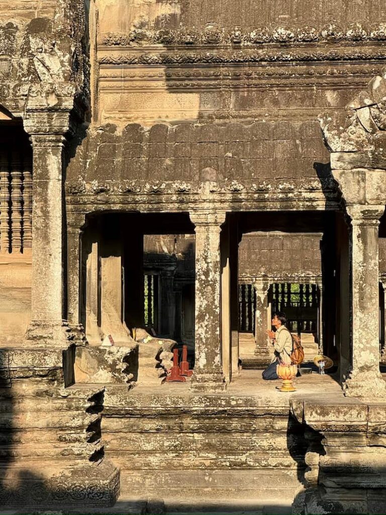A person praying against golden Buddha on the upper tier courtyard during a 2-day Angkor Wat tour.