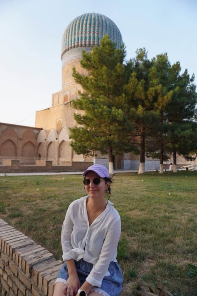 Relaxing in a park with the iconic blue dome of the Bibi-Khanym Mosque and green trees in the background.