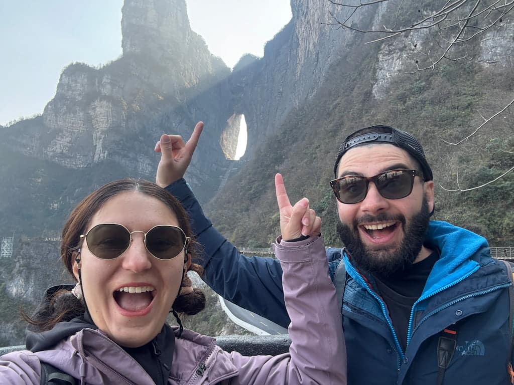 Eleni and Alessandro pointing their finger to the Tianmen mountain mountain hole and smiling to the camera, in China