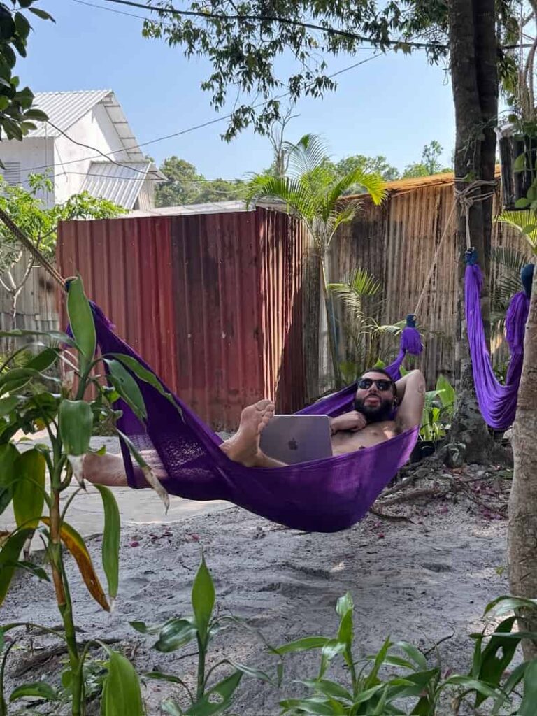 Ale relaxing in a purple hammock outdoors with a laptop on a tropical island getaway.