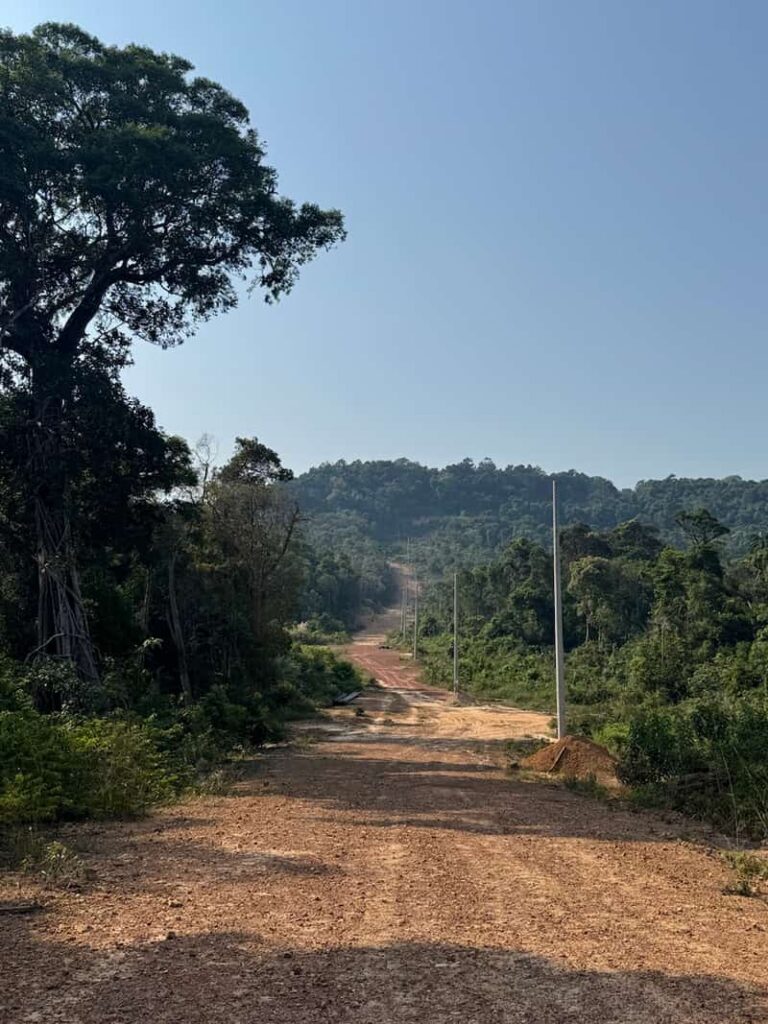 A wide dirt road cutting through lush green jungle and hills under a clear blue sky on Koh Rong Sanloem.