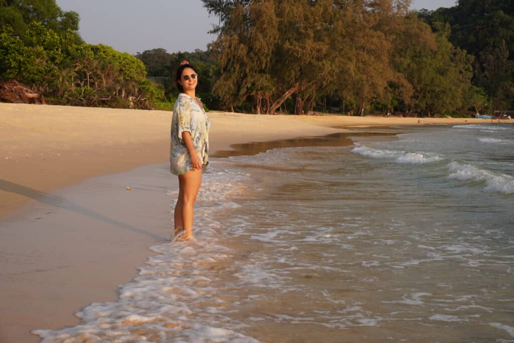 Eleni standing in the shallow waves at Lazy Beach on Koh Rong Sanloem, Cambodia, with golden sand and lush trees in the background.