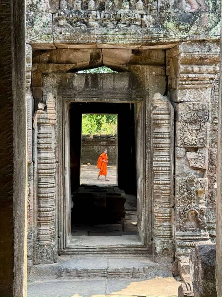 A Buddhist monk in orange robes walks through a series of ancient stone doorways.