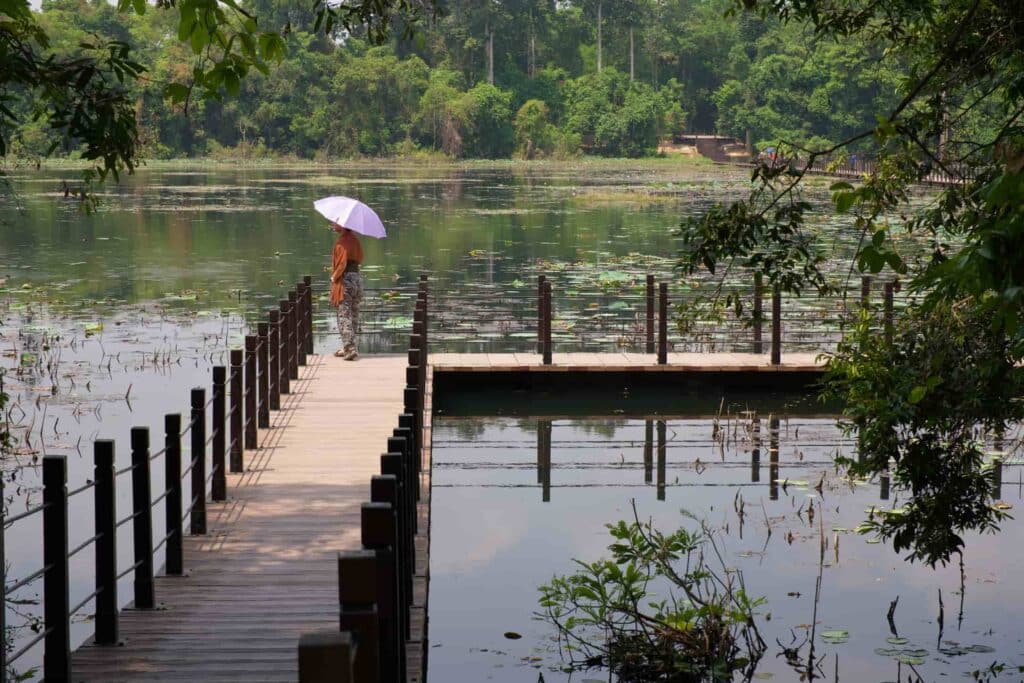 Traveller carrying a pink umbrella and enjoying the lakeside close to Neak Poan temple, in Siem Reap