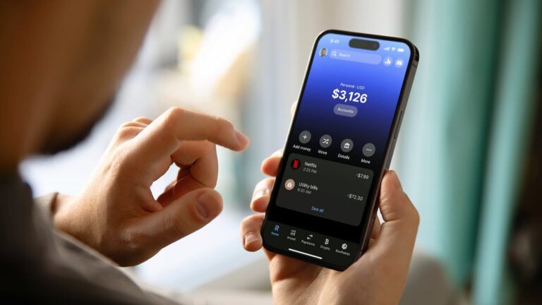 A person holding a smartphone showing the Revolut mobile banking app interface to track expenses and save money for travel.