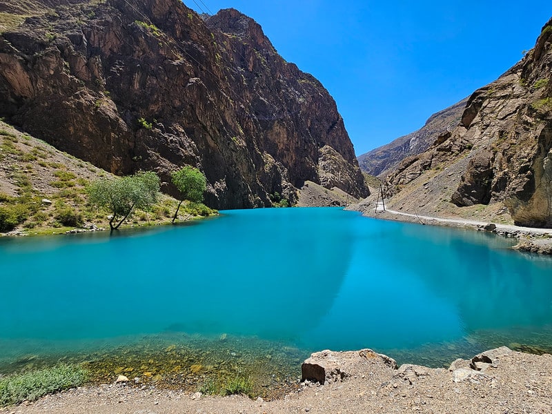 Clear blue water of one of the Seven Lakes in Tajikistan, set against a backdrop of rugged, rocky mountains.