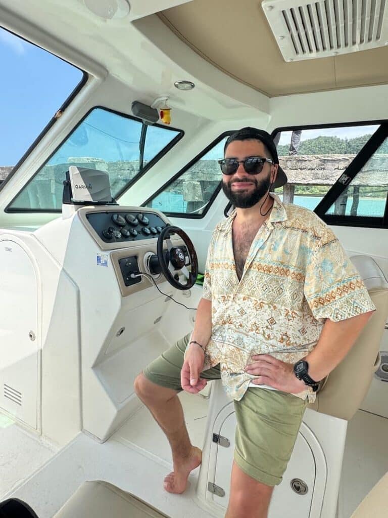 A smiling man posing at the helm inside the cockpit of a ferry during an island boat trip from Sihanoukville.
