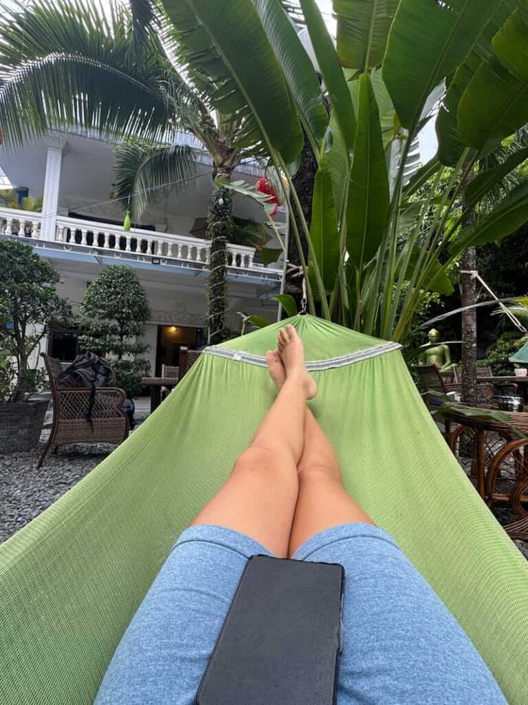 Point-of-view shot of Eleni resting her legs and phone in a green hammock surrounded by lush tropical plants at a hotel in Sihanoukville.