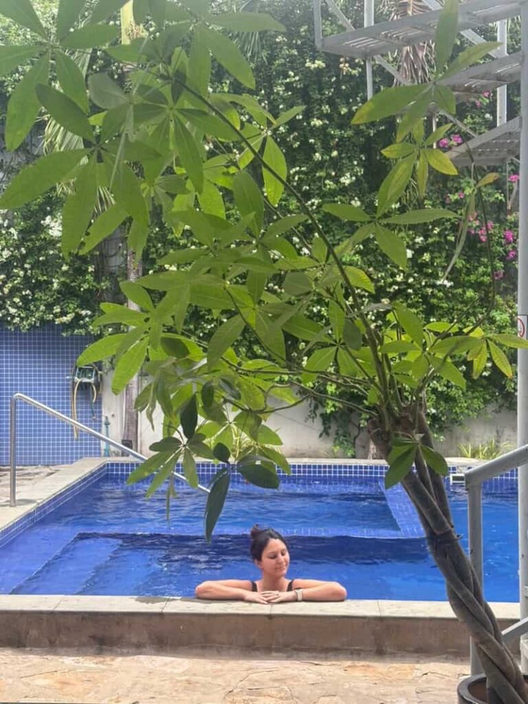Eleni relaxing in a blue-tiled swimming pool surrounded by tropical foliage at a hotel in Sihanoukville.