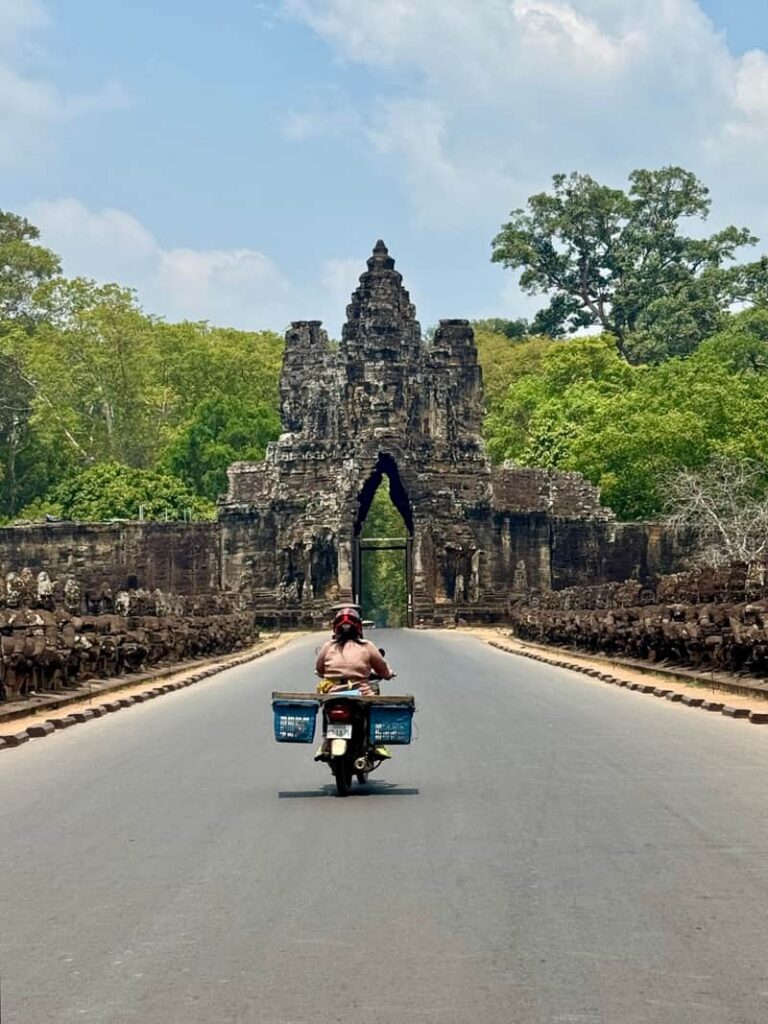 Motorbike rider approaching the historic stone South Gate of Angkor archaeological park in Cambodia.