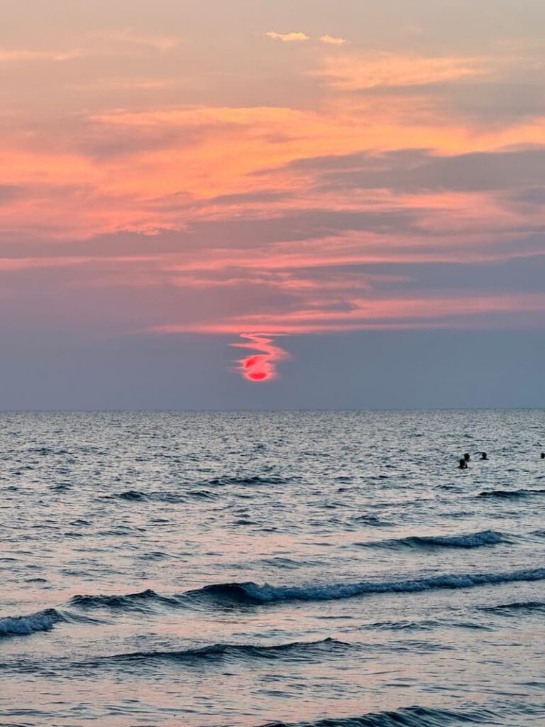 Vibrant pink and orange sunset glowing through hazy clouds over the ocean waves at Koh Chang.