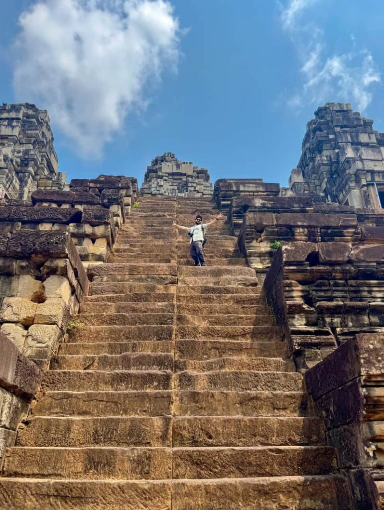 Traveler walking up the steep pyramid steps and enjoying the ancient stone architecture at Ta Keo temple in Cambodia.