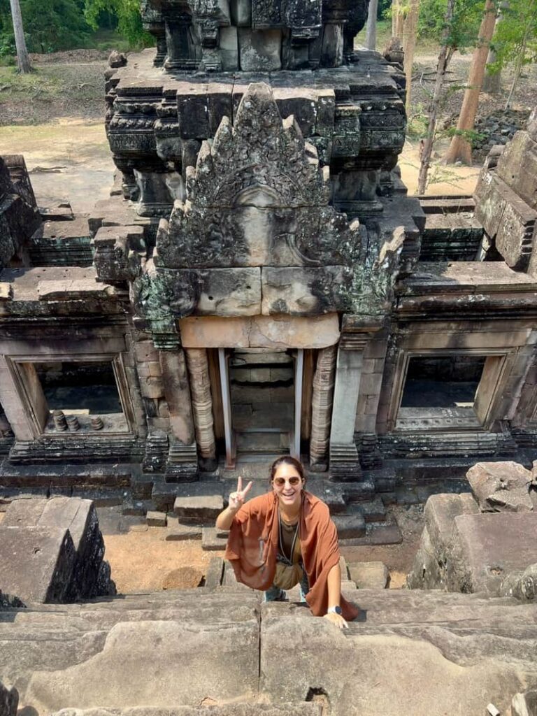 Traveler scaling the steep pyramid steps and ancient stone architecture at Ta Keo temple in Cambodia.