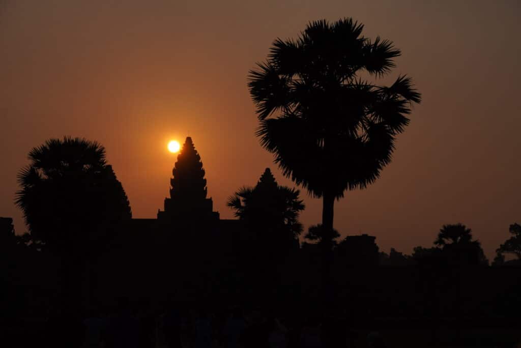 The sun rising directly behind the silhouetted central tower and palm trees of Angkor Wat.