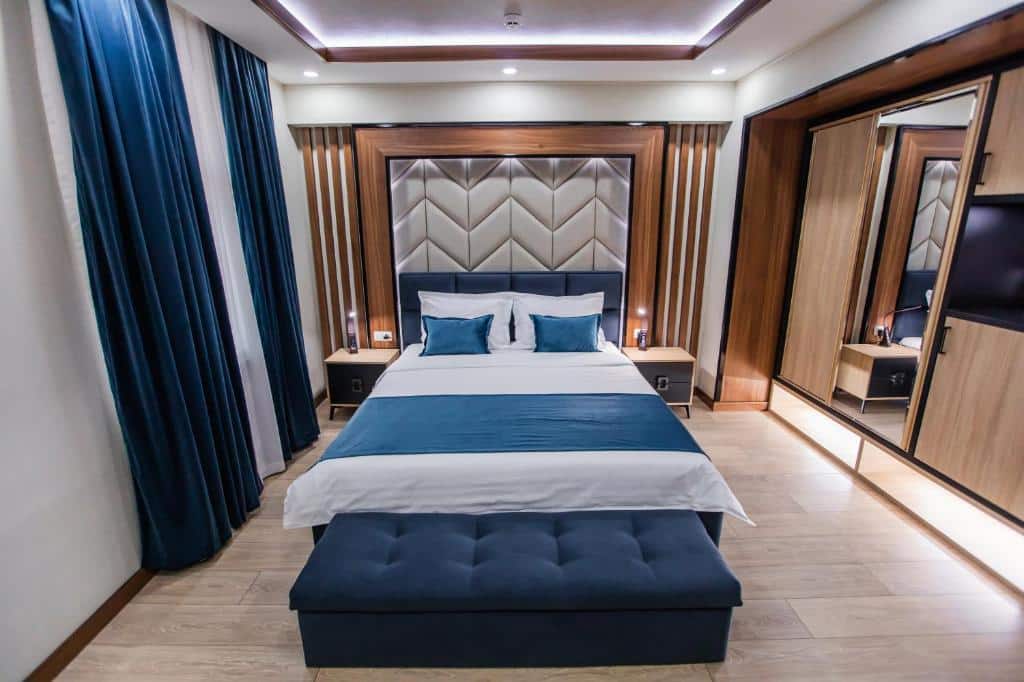 Modern hotel room at Art Deluxe Hotel in Tashkent featuring a double bed with blue accents, wooden headboard, and a mirrored wardrobe.