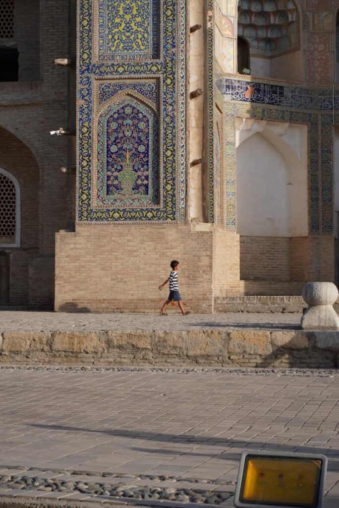 A young boy walking past an intricately tiled historical building in Bukhara, in Uzbekistan.