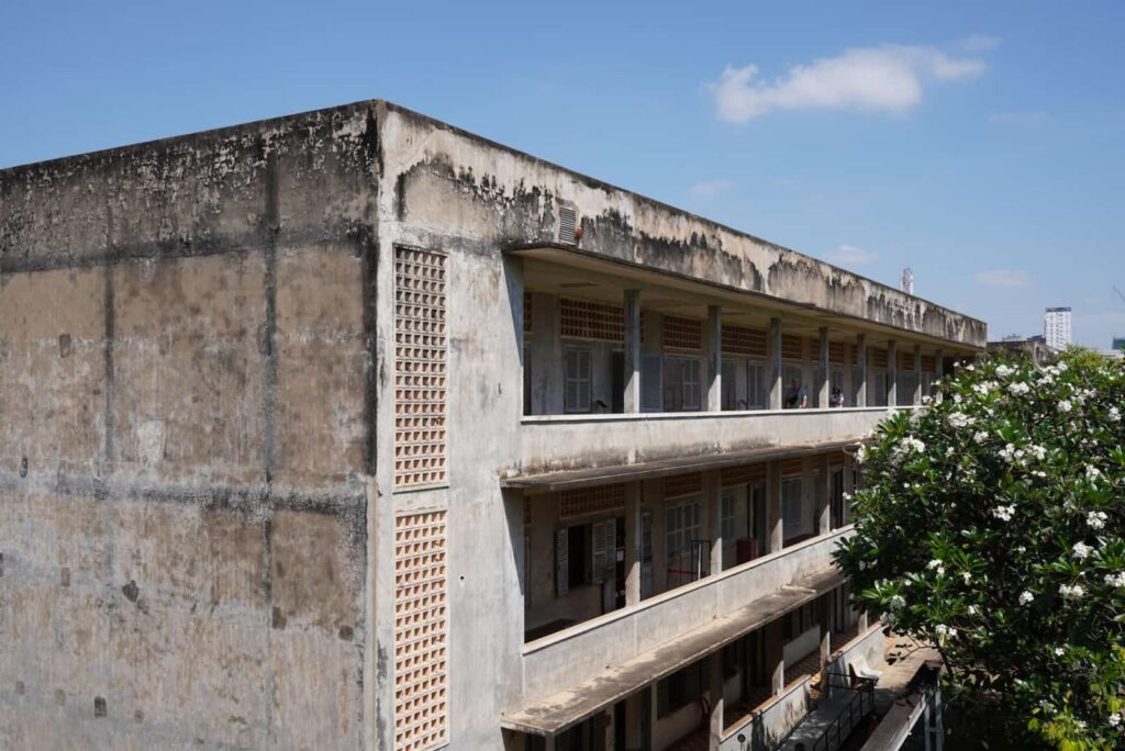Exterior perspective view of Building B at the Tuol Sleng Genocide Museum showing its multi-story balconies and weathered concrete facade.