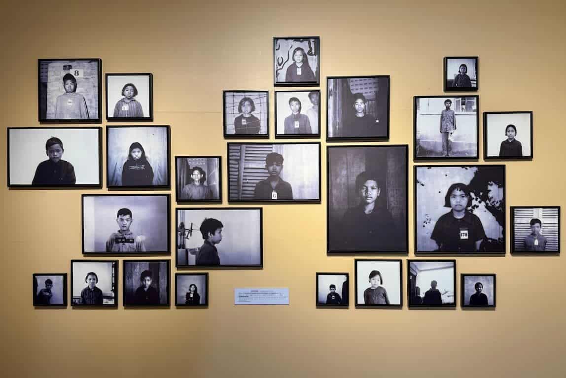 A museum wall displaying a collection of framed black-and-white portrait photographs of young victims from S-21 prison.