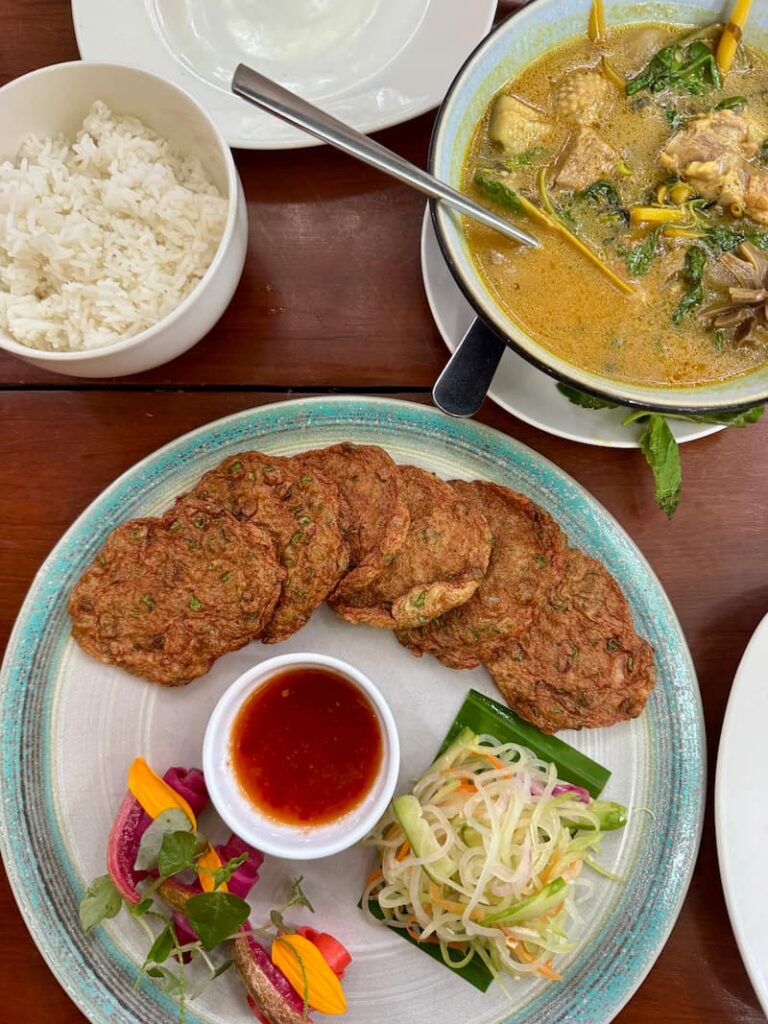 Traditional Cambodian meal at Eleven One Kitchen featuring golden fish cakes with sweet chili sauce, a bowl of aromatic yellow curry, and steamed white rice.