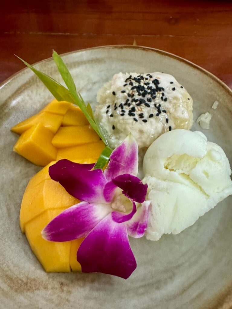 Mango sticky rice dessert served with a scoop of ice cream, black sesame seeds, and a fresh purple orchid flower at Eleven One Kitchen.