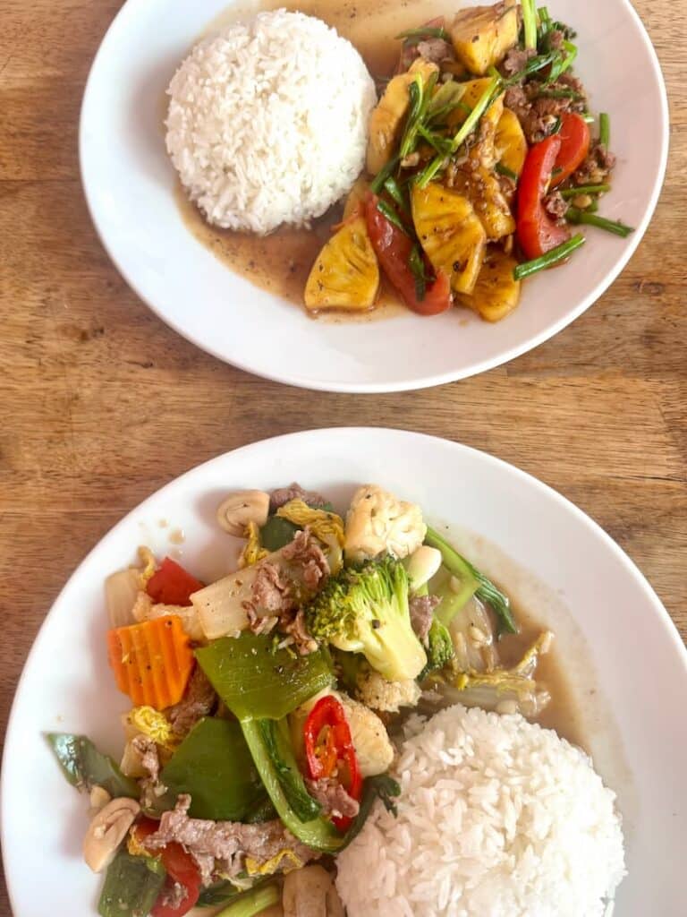 Plates of traditional Cambodian food featuring stir-fried meat with pineapple, fresh vegetables, and white rice.