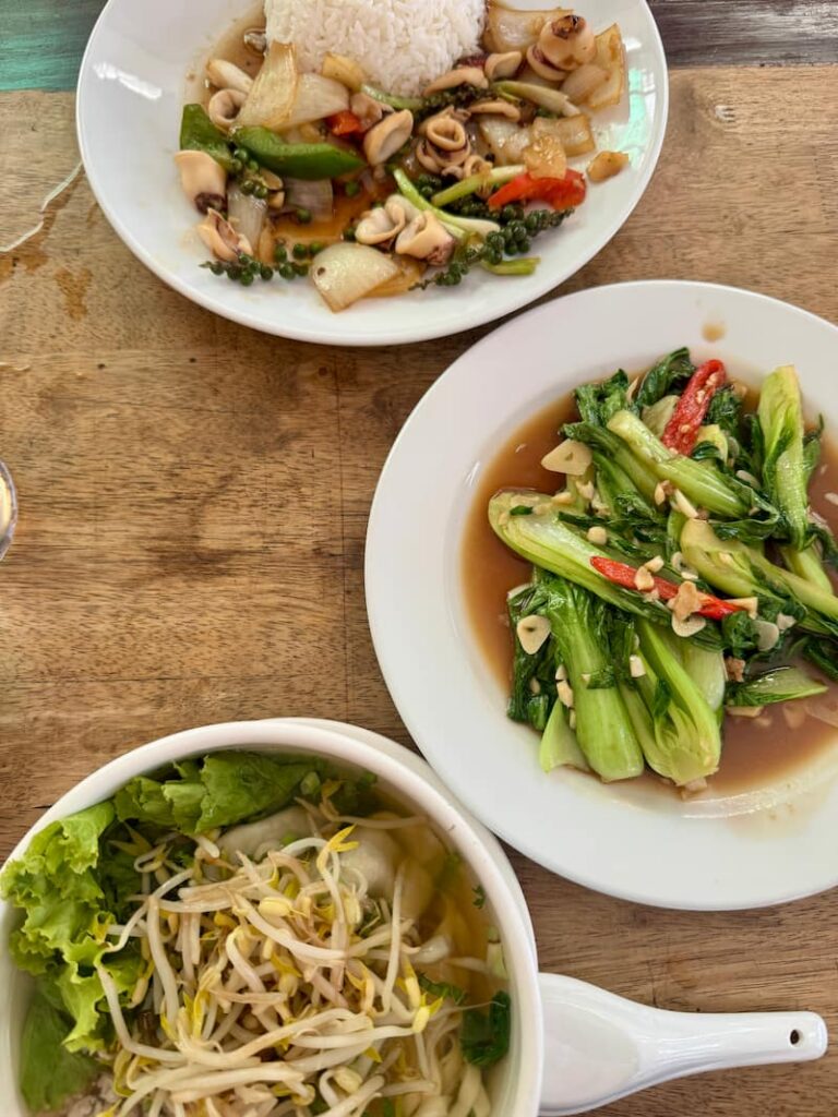 Dishes from Kengkong Restaurant including stir-fried squid with green peppercorns, garlic stir-fried greens, and a bowl of noodle soup on a wooden table.