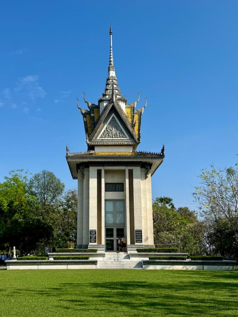 The towering memorial stupa at the Choeung Ek Killing Fields against a clear blue sky.