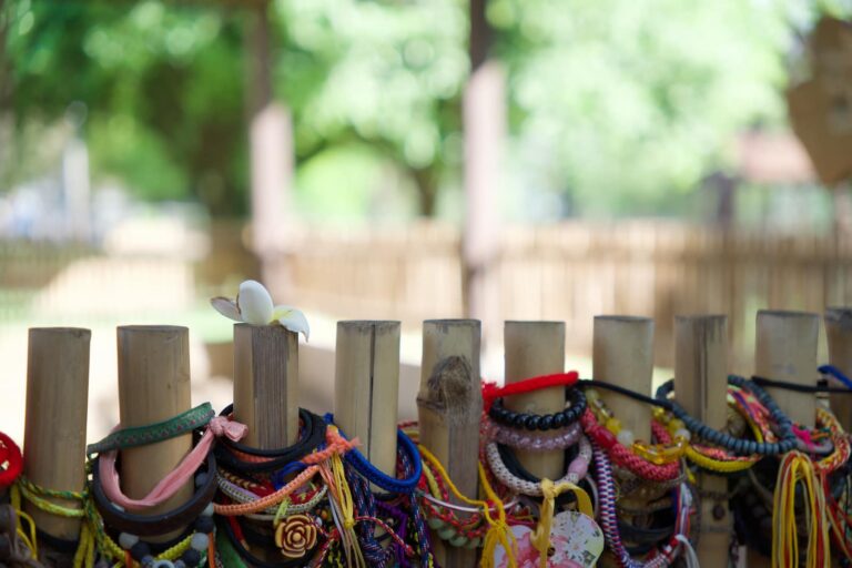 Close-up of a single white flower resting on a bamboo fence decorated with memorial bracelets at the Killing Fields.