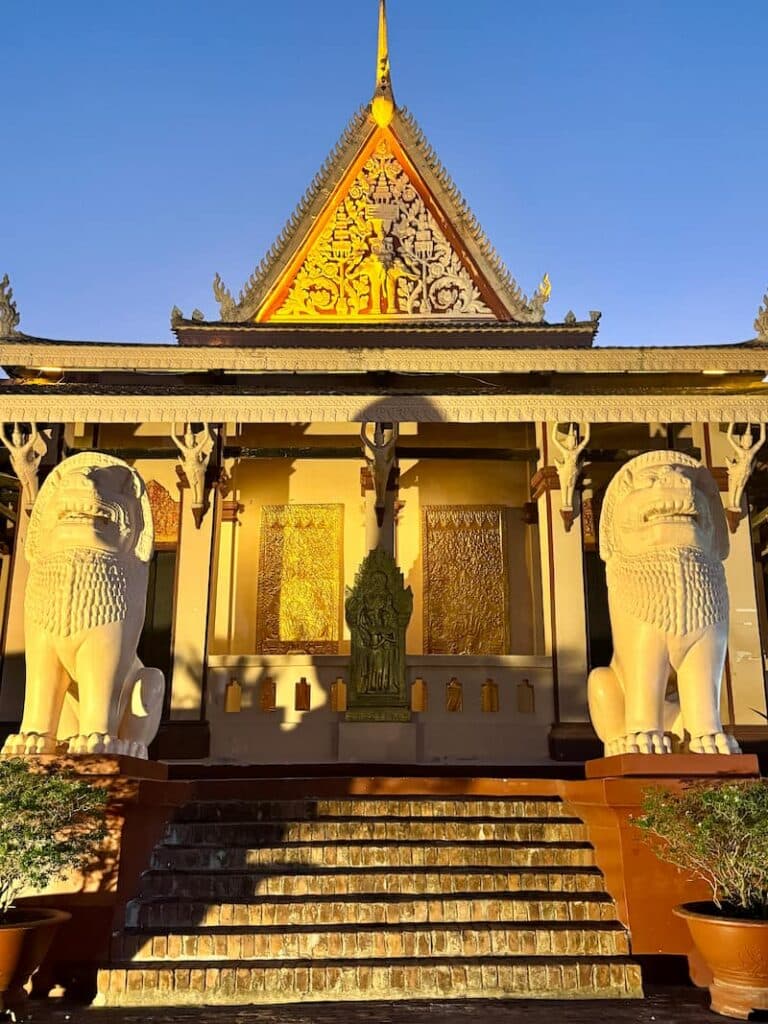 An illuminated temple building featuring large white lion statues guarding the steps and a glowing golden gable roof under a clear evening sky.