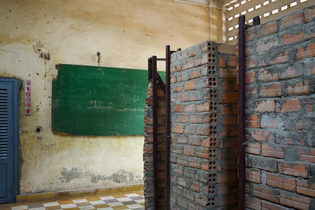 Rough brick cell partitions inside a former classroom with a green chalkboard at Tuol Sleng Genocide Museum (S-21) in Phnom Penh, Cambodia.