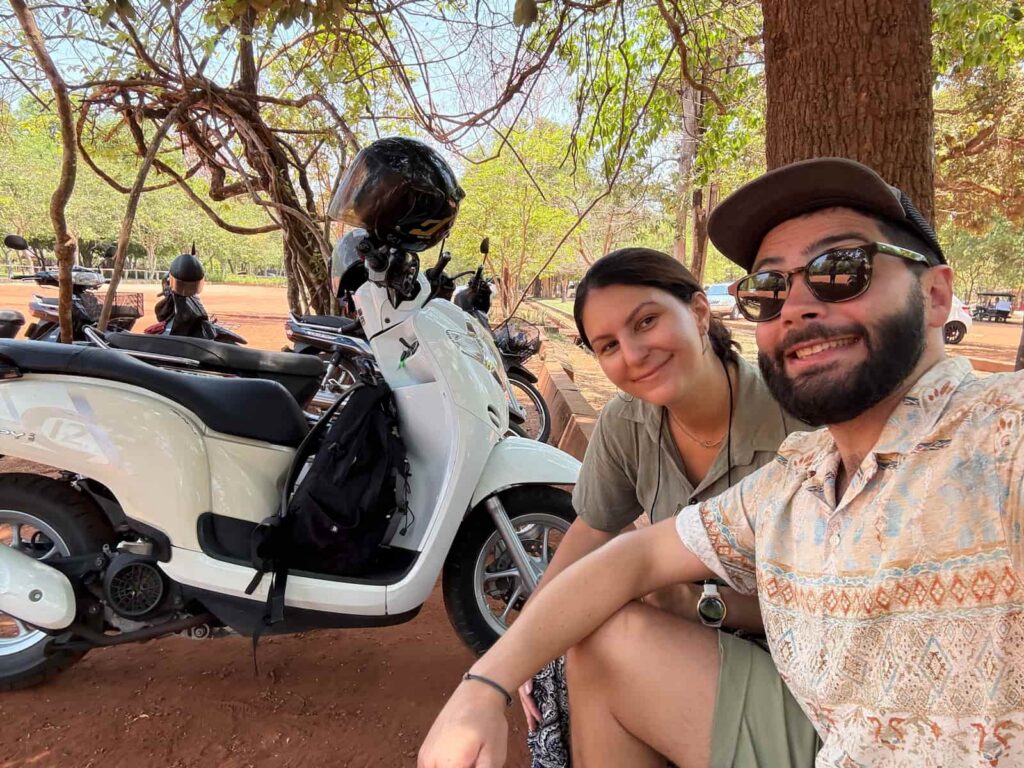 Travelers posing next to a rented white scooter outdoors, featured in our Cambodia transport guide