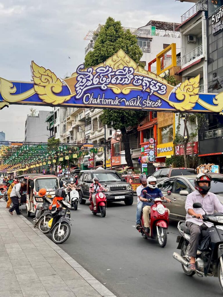 Bustling street traffic with scooters and cars passing under the Chaktomuk Walk Street sign as featured in our Cambodia transport guide
