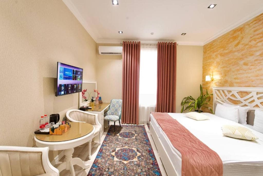 Comfortable room at Silk Road Empire Hotel in Samarkand featuring a double bed, traditional oriental rug, desk, and a wall-mounted TV.