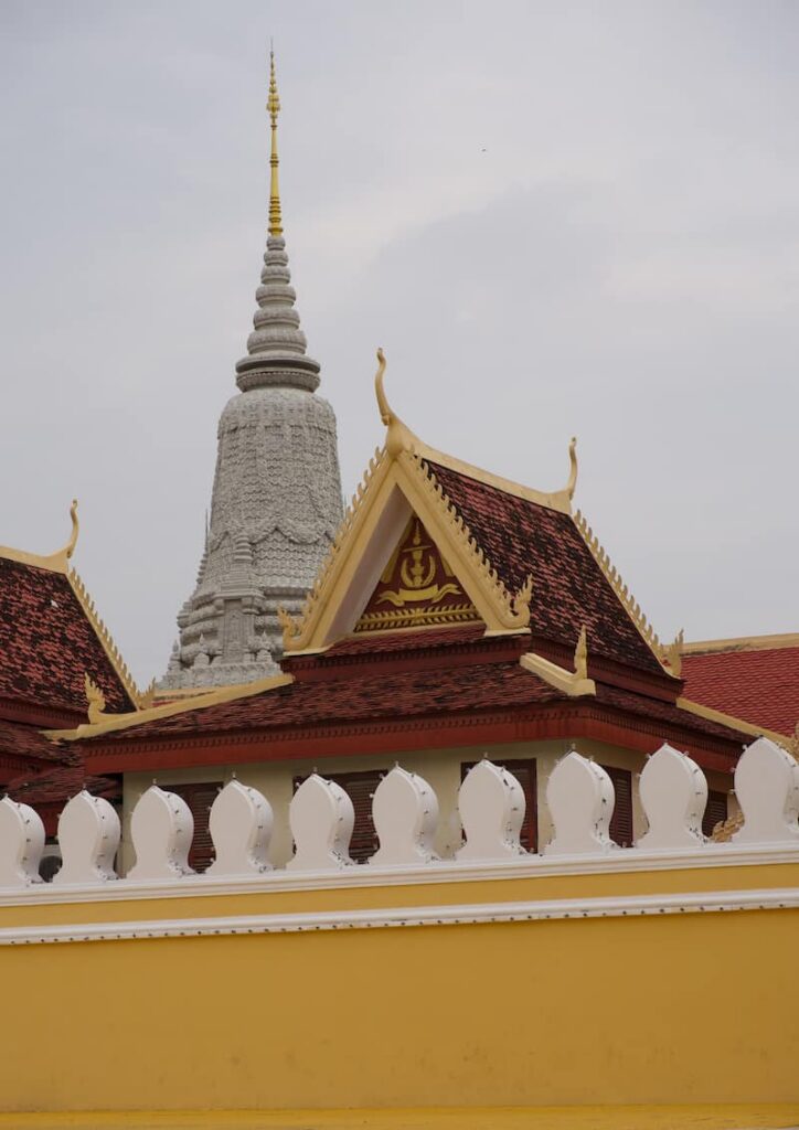 The ornate stupa of the Silver Pagoda rising behind traditional red-tiled temple roofs and a decorative white wall at the Royal Palace complex in Phnom Penh.
