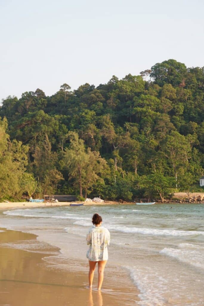 One of the authors of this blog walking along the sandy shore of Sunset Beach with a lush green tropical jungle backdrop.