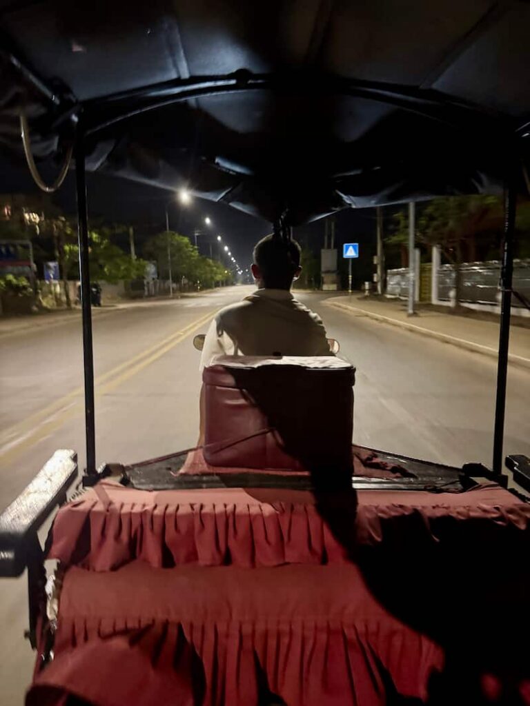 Night view from the back of a tuk-tuk riding down a lit street, highlighted in our Cambodia transport guide