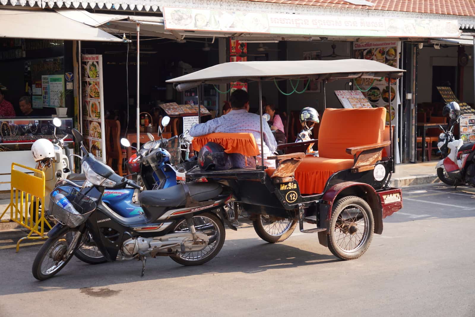 Cambodian remork (tuk-tuk) parked on a street with motorbikes in Siem Reap